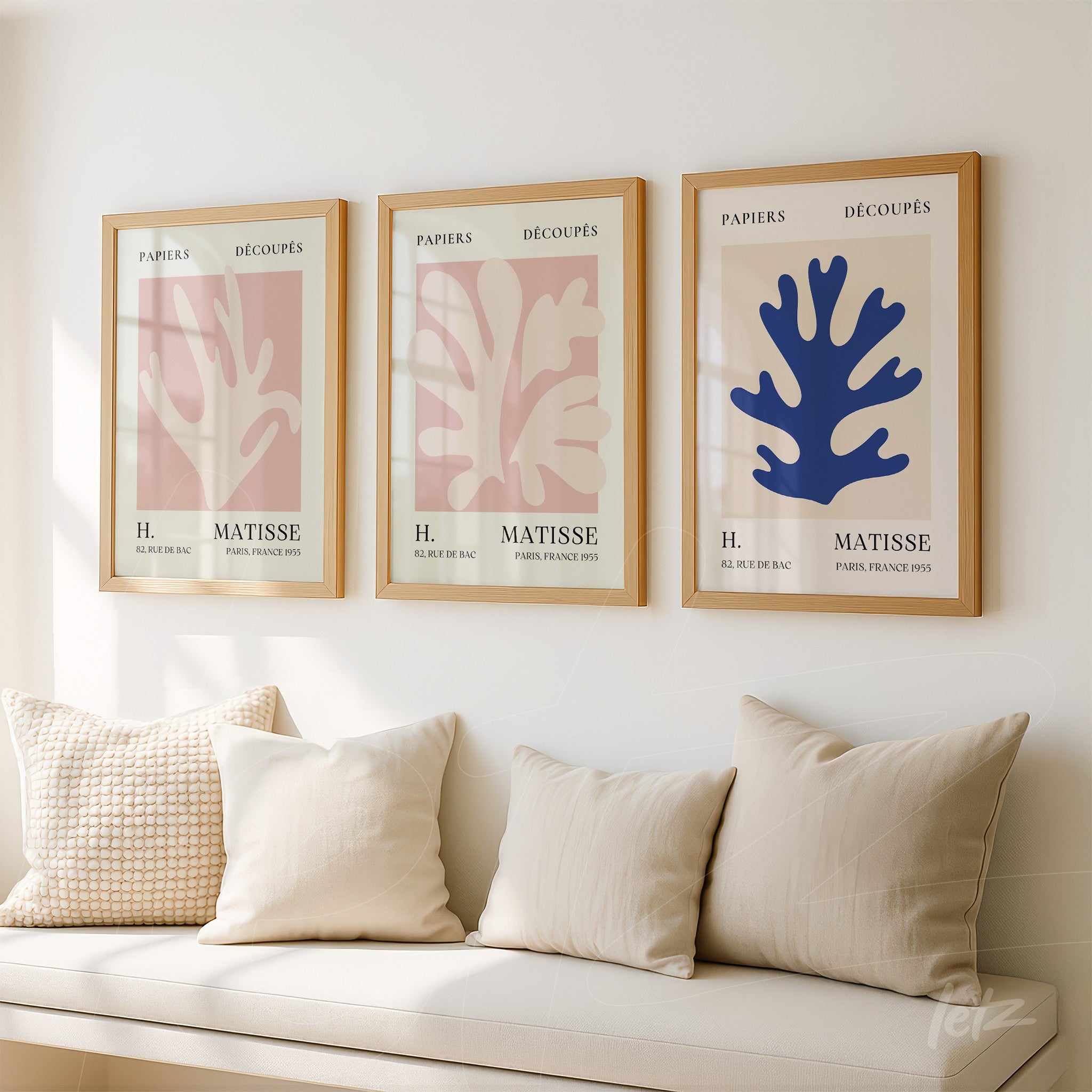 composition of three framed wall art pieces featuring modern leaf illustrations in pastel colors with light frames displayed on a neutral wall alongside a cozy sofa in the foreground