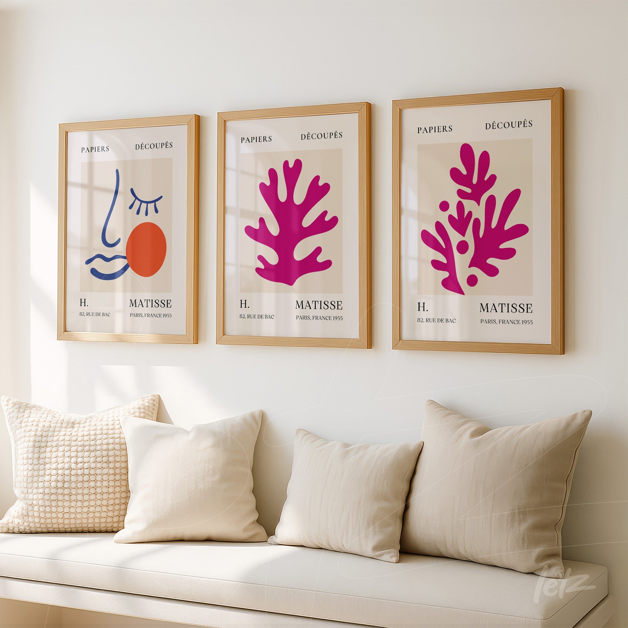 collection of three framed artworks featuring abstract illustrations in shades of pink and orange with neutral backgrounds and cream-colored cushions on a sofa