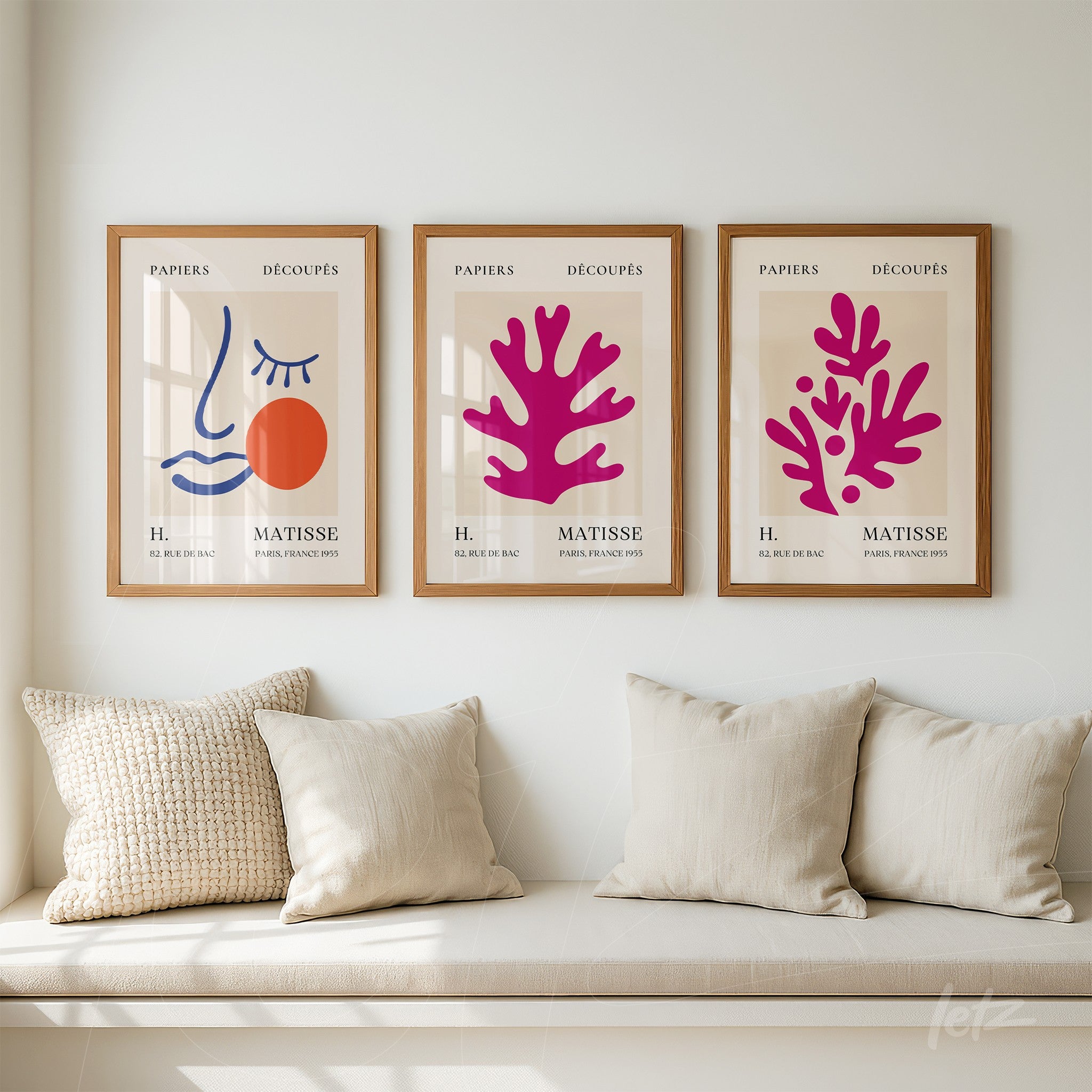 composition of three framed abstract wall art pieces in light wood, featuring a minimalist face, organic pink shapes, and a graphic design in blue and orange, displayed on a light wall