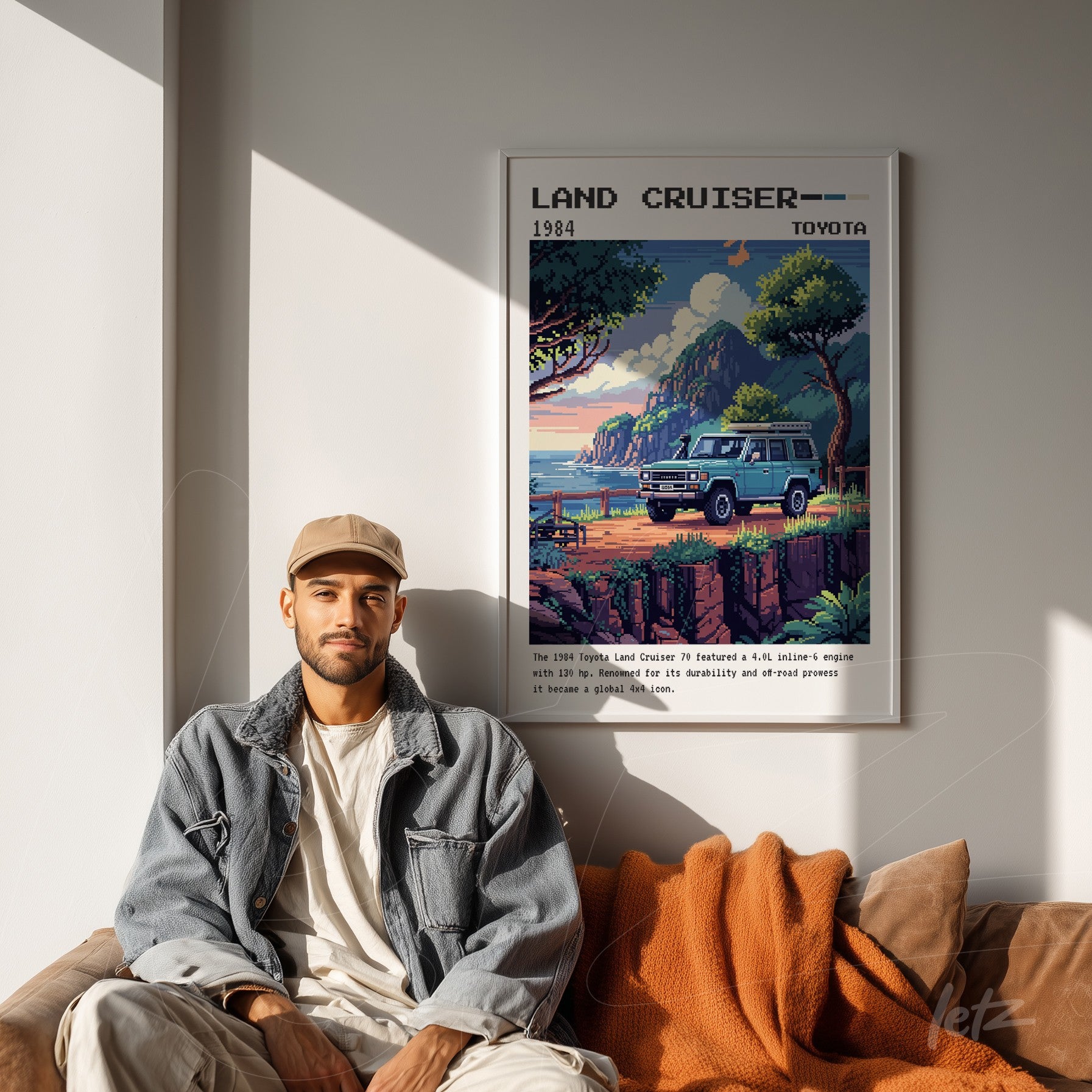 framed vintage style illustration of the 1984 Toyota Land Cruiser displayed on a light wall beside a man sitting on a sofa with an orange blanket