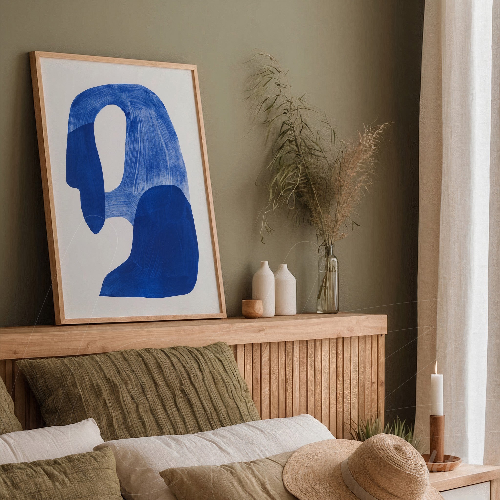 abstract wall art featuring blue shapes in a light wood frame displayed above a wooden bed headboard with earthy tone cushions