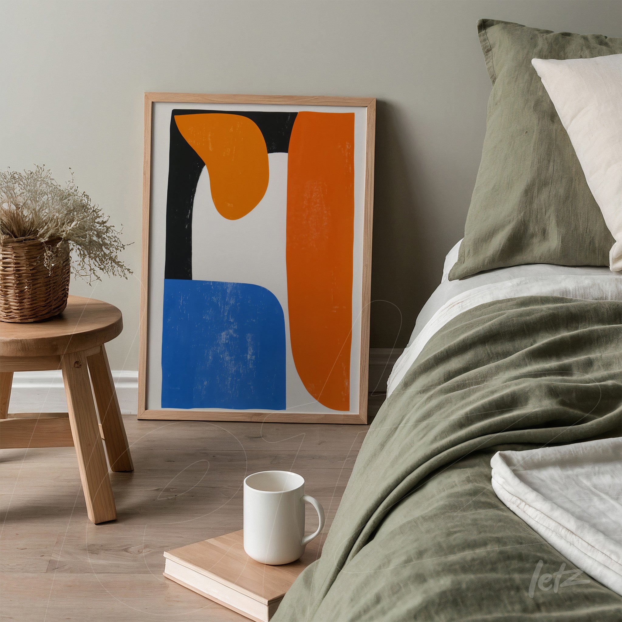 framed abstract artwork in orange, blue, and white displayed on a wooden side table next to a bed with neutral-toned bedding