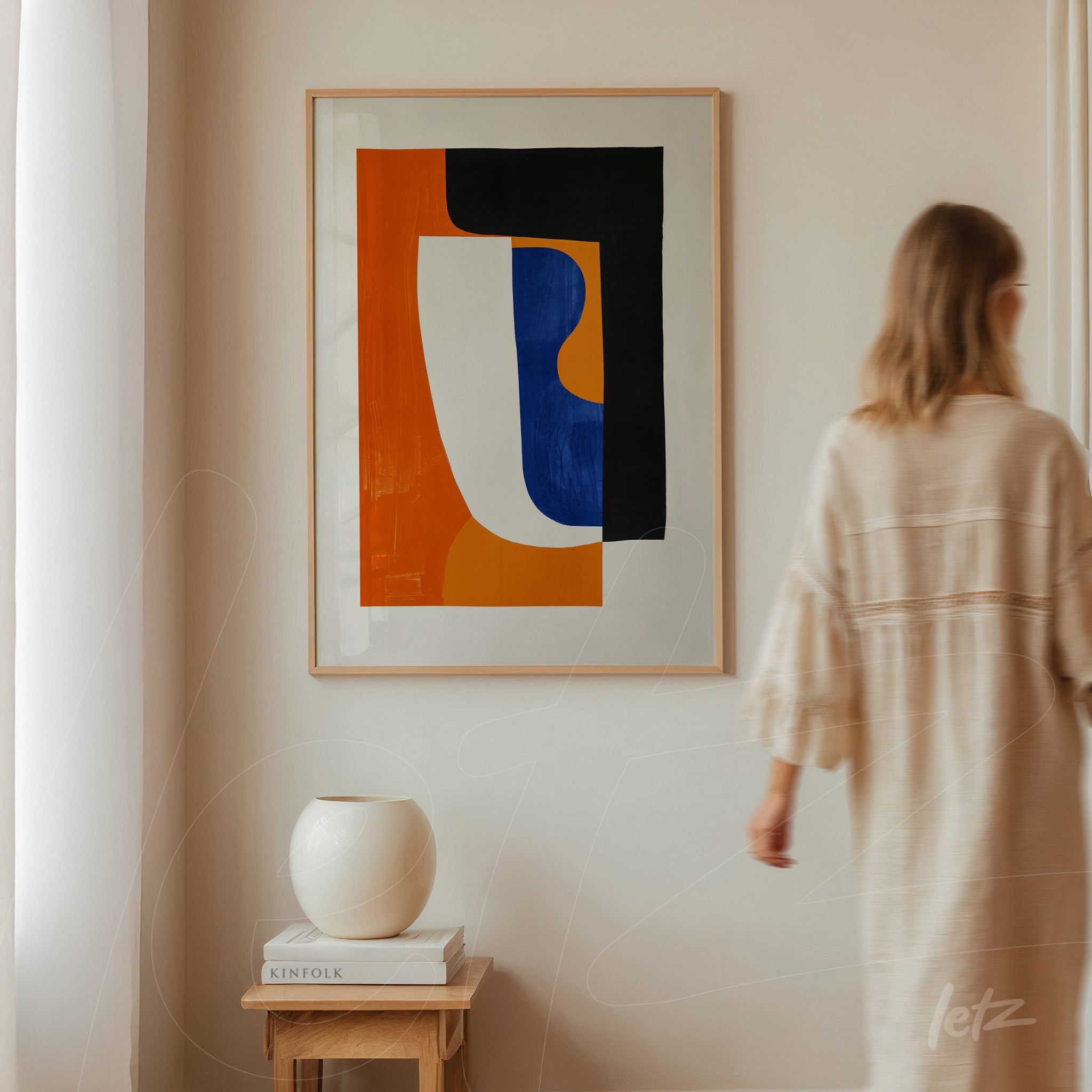 abstract artwork featuring geometric shapes in black, orange, and blue, in a light frame, displayed on a neutral wall next to a vase