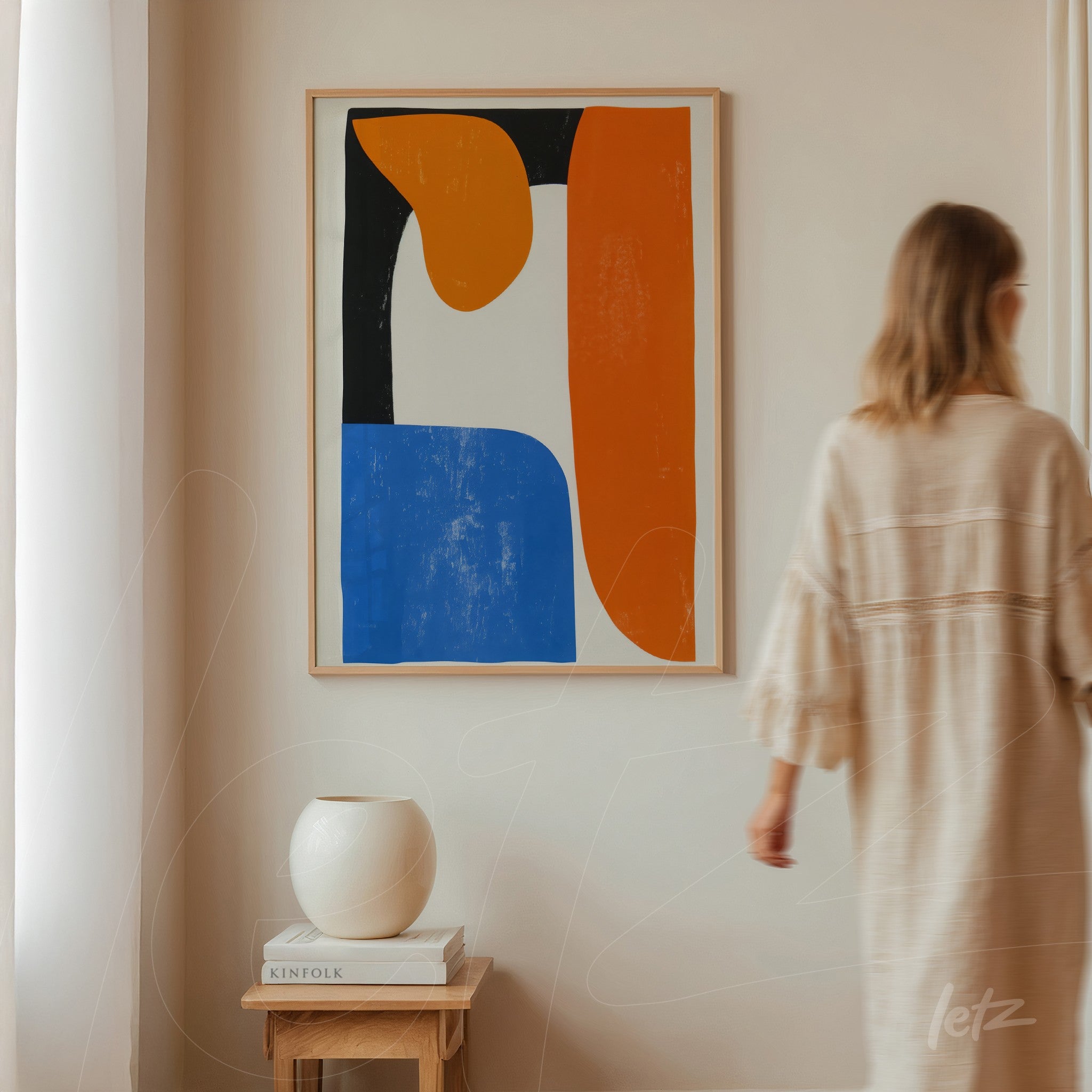 abstract wall art in light frame featuring geometric shapes in orange, blue, and black displayed on neutral wall next to white vase