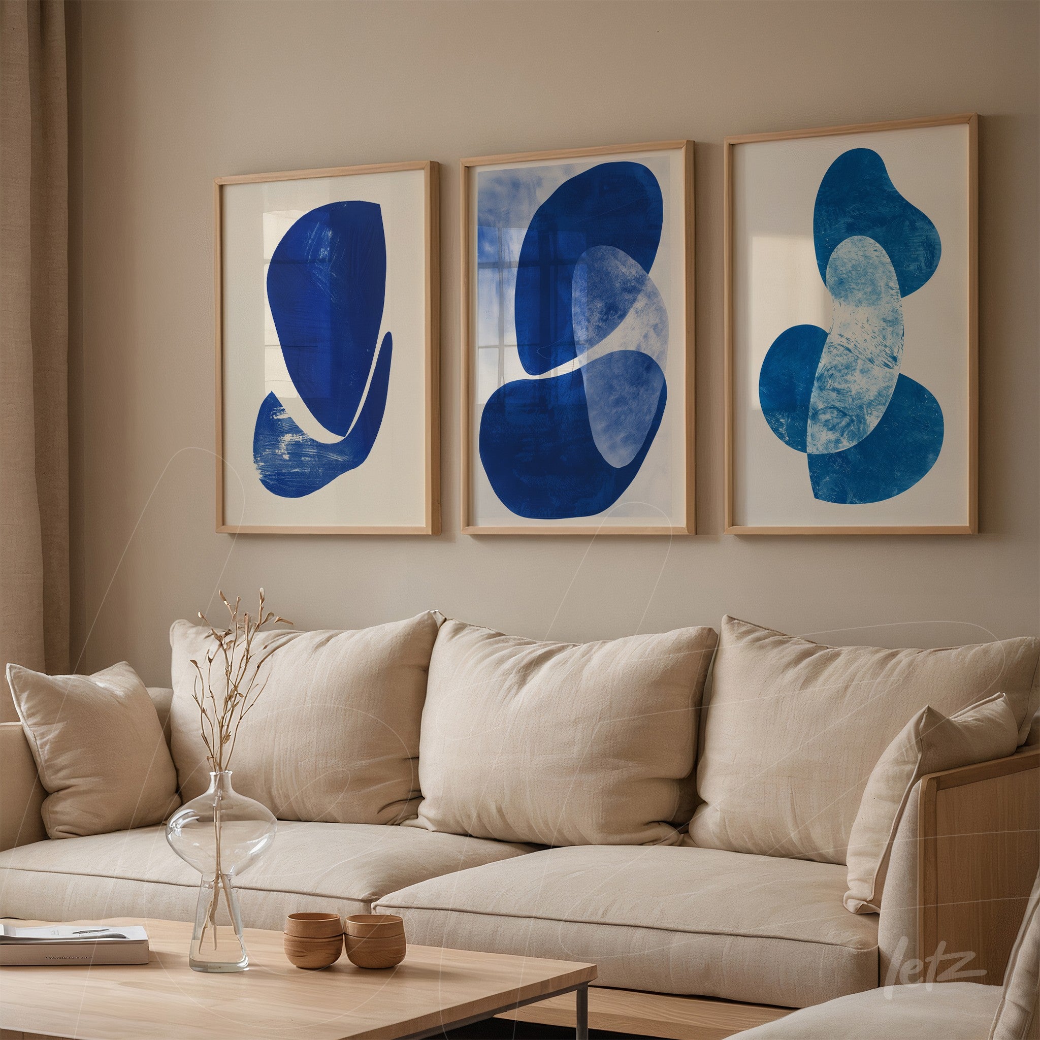 set of three abstract wall art pieces featuring blue shapes in light wood frames against a neutral wall