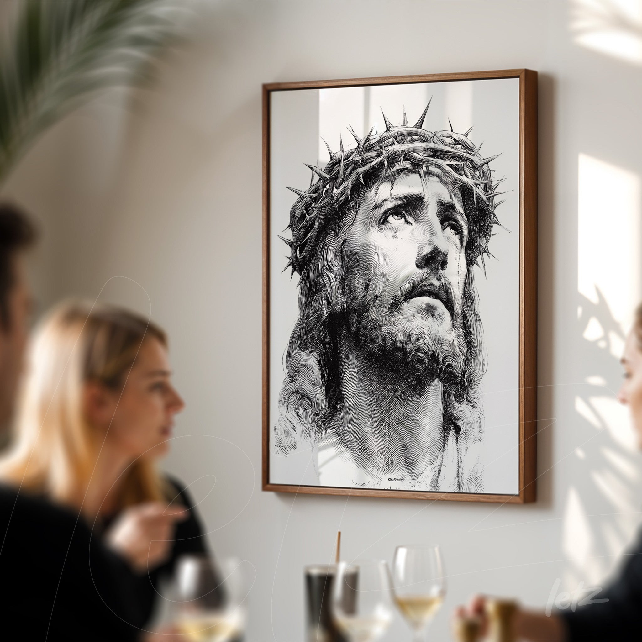 framed artwork depicting the face of Christ with a crown of thorns displayed on a light wall with people in a social setting in the background