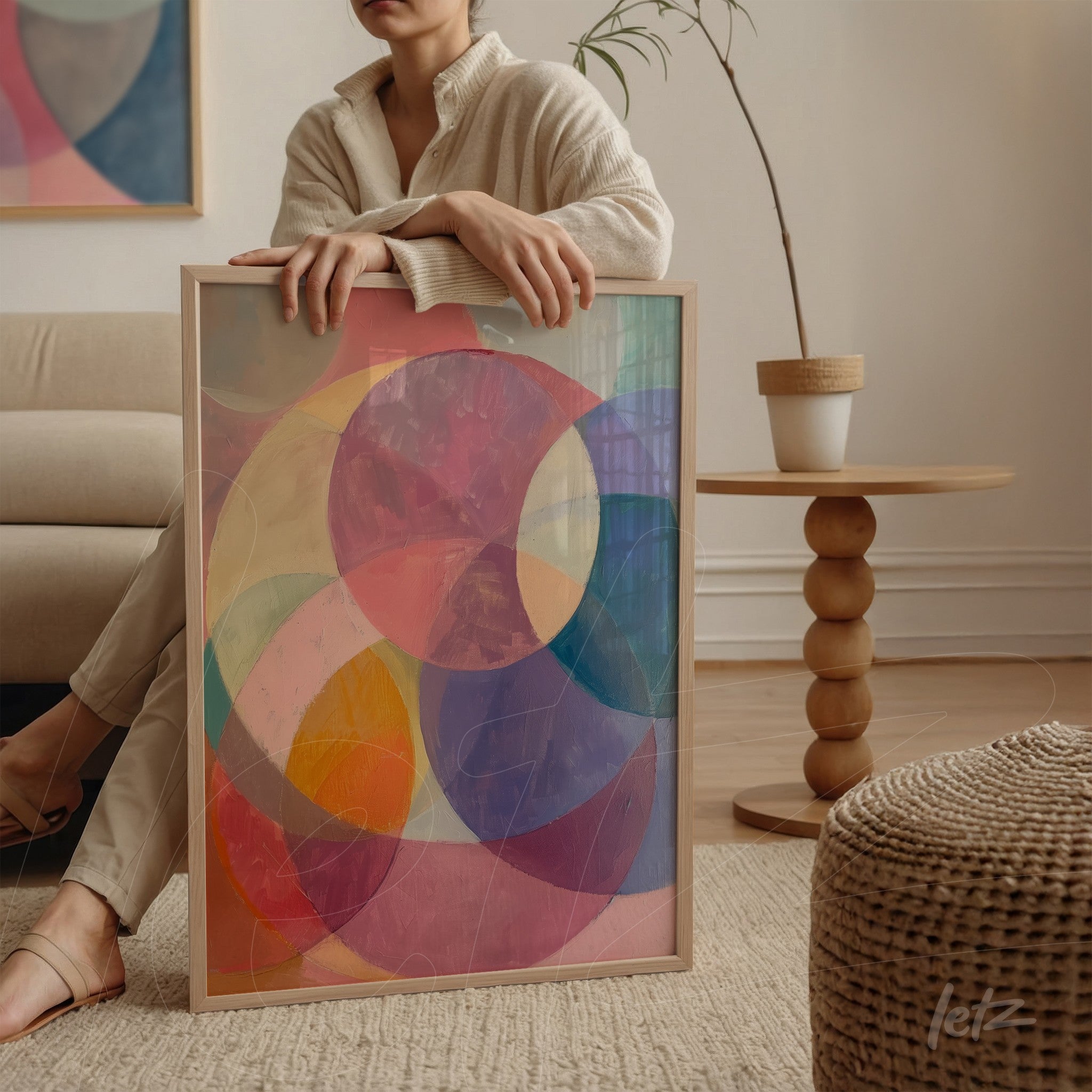 framed wall art featuring abstract design with colorful circles on pink background displayed by a woman in a minimalist setting