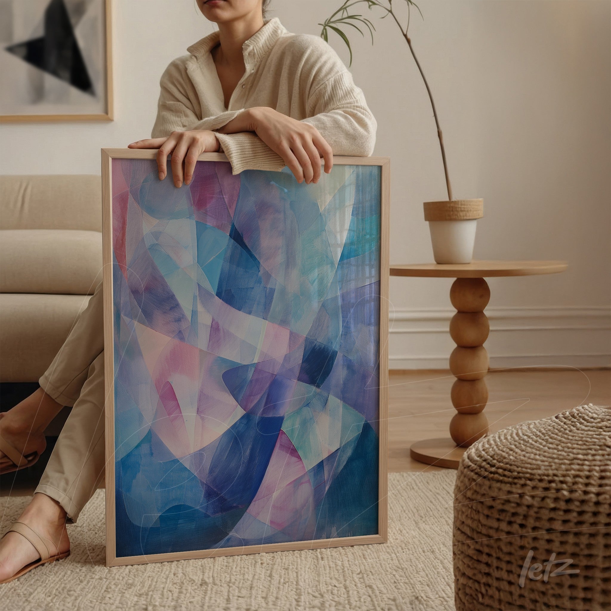 abstract art in light wood frame featuring dominant shades of blue, pink, and lavender leaning next to a chair in a bright room