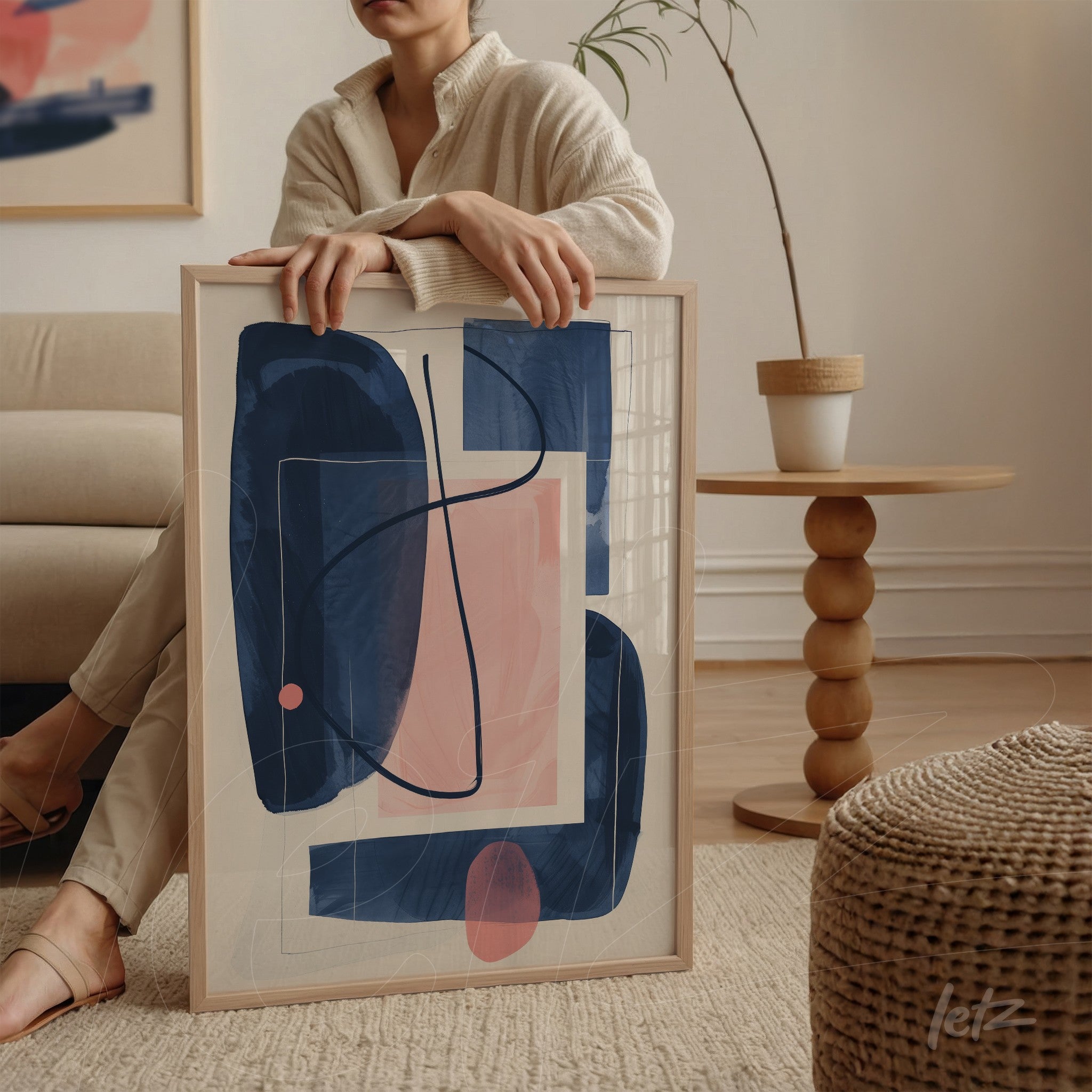 framed abstract artwork in shades of blue and pink, light frame, leaning against a chair, detail of wooden table in the background