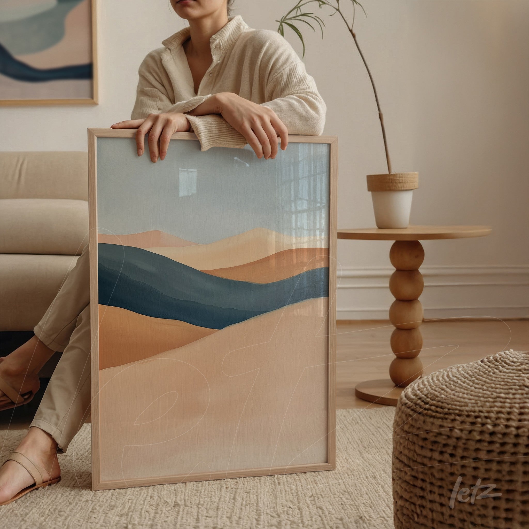 framed abstract art in neutral tones and blue, held by a woman in a well-lit room