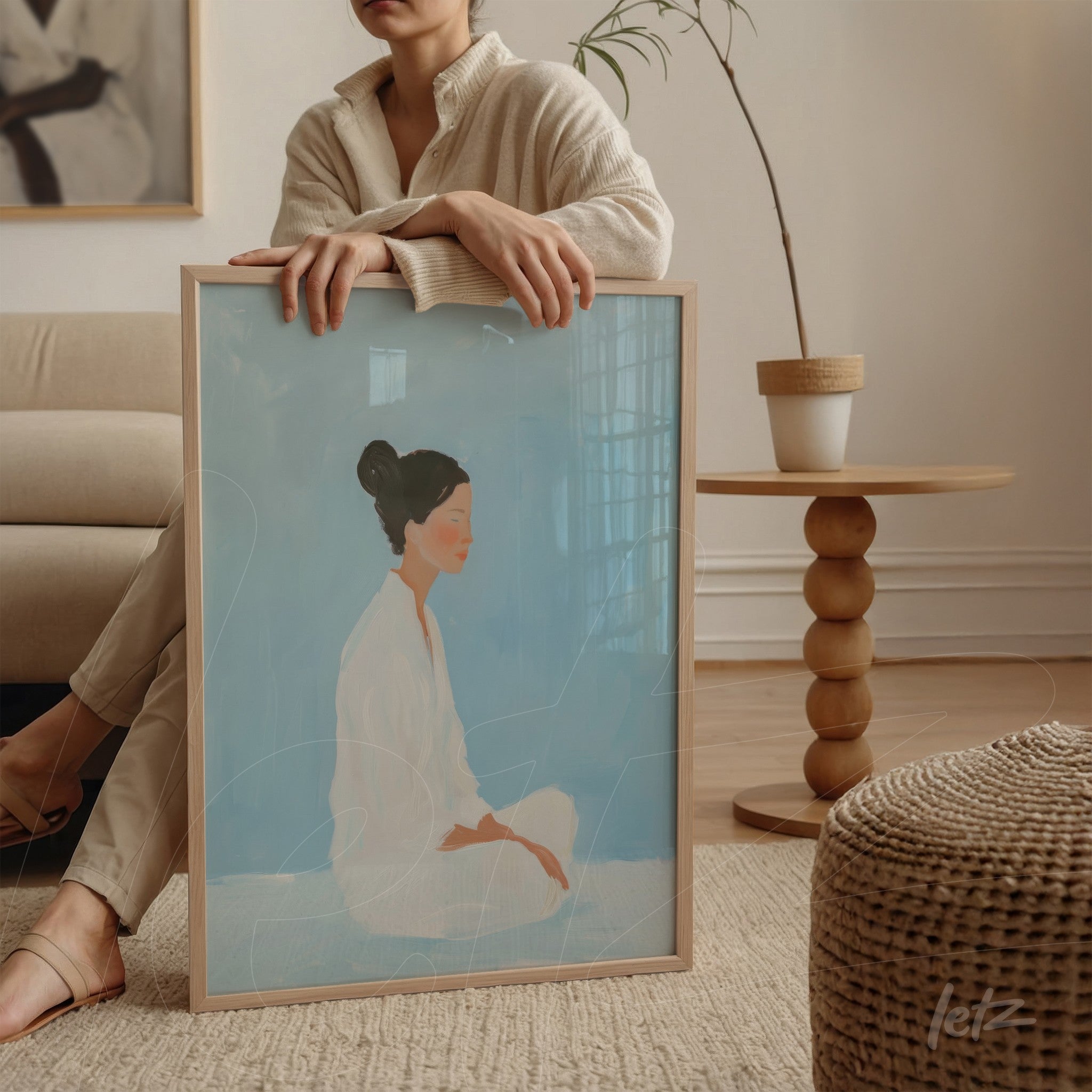 framed wall art featuring a minimalist illustration of a seated woman against a soft blue background, displayed on a round side table