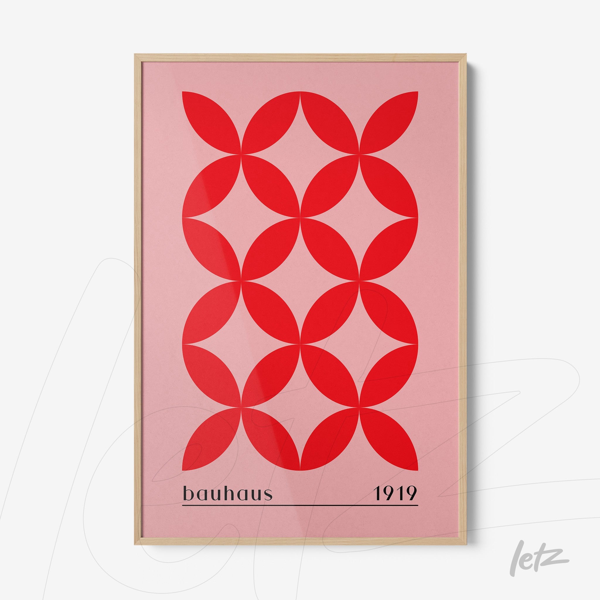 poster featuring red geometric shapes on a pink background framed in light wood with text referencing bauhaus 1919