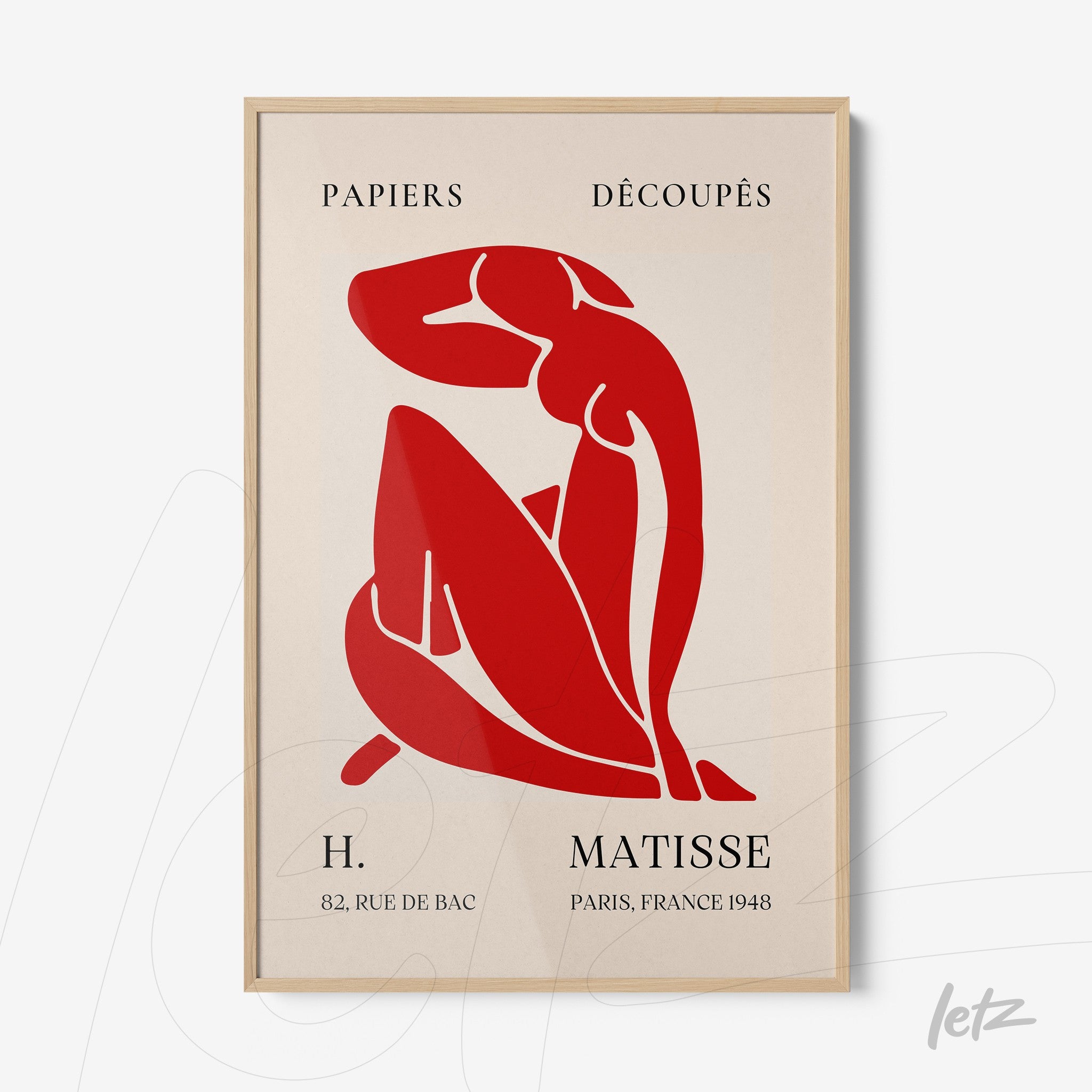 framed wall art featuring abstract red artwork of a female figure in a curled pose with light wood frame and neutral background