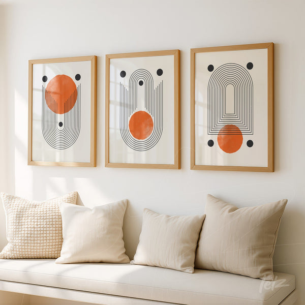 série de três quadros com arte abstrata em molduras de madeira clara, apresentando padrões de linhas pretas e formas laranjas, expostos sobre parede branca acima de sofá com almofadas claras