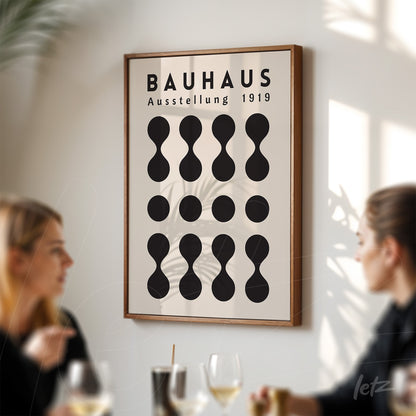 poster print featuring geometric Bauhaus design in wooden frame, displayed on a light wall with people in foreground