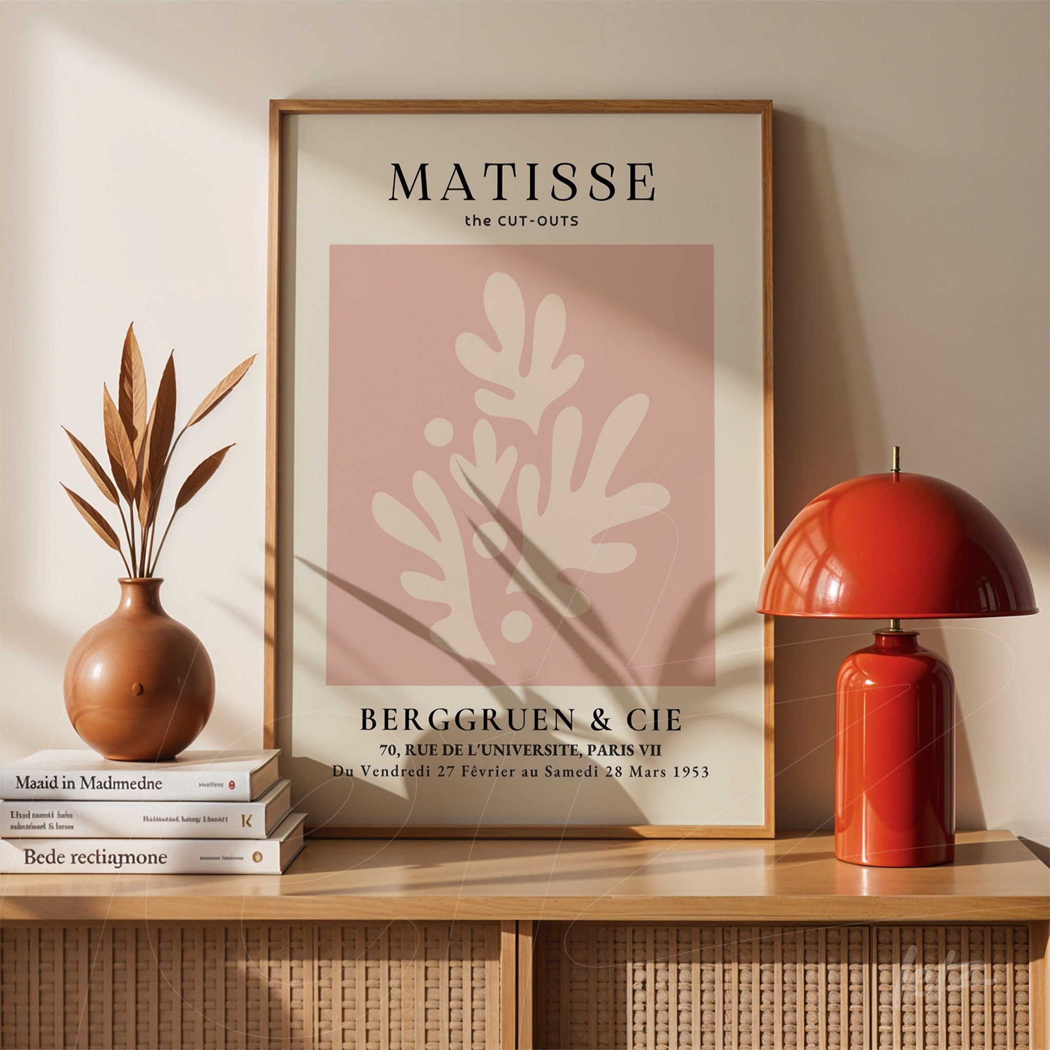 framed abstract art of leaves with pink background displayed on a wooden shelf next to a vase and a lamp