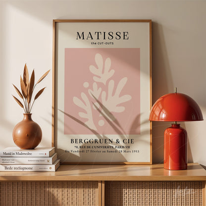 framed abstract art of leaves with pink background displayed on a wooden shelf next to a vase and a lamp