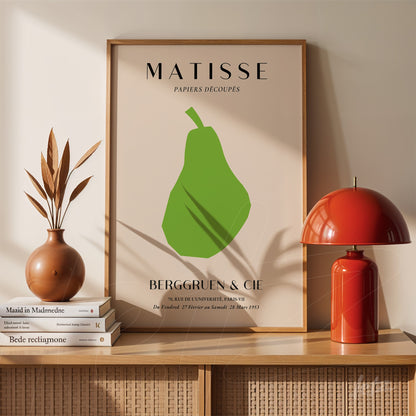 decorative artwork featuring a modern green pear illustration with a simple light wood frame and beige background displayed on a shelf with vases and books
