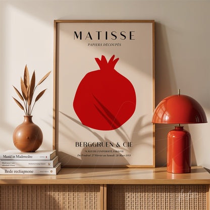 decorative framed art featuring a pomegranate silhouette on light background, displayed in a room with vases and a red lamp