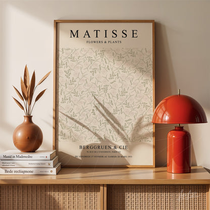 framed wall art of matisse flowers and plants with light wood frame displayed on a table with a vase and red lamp