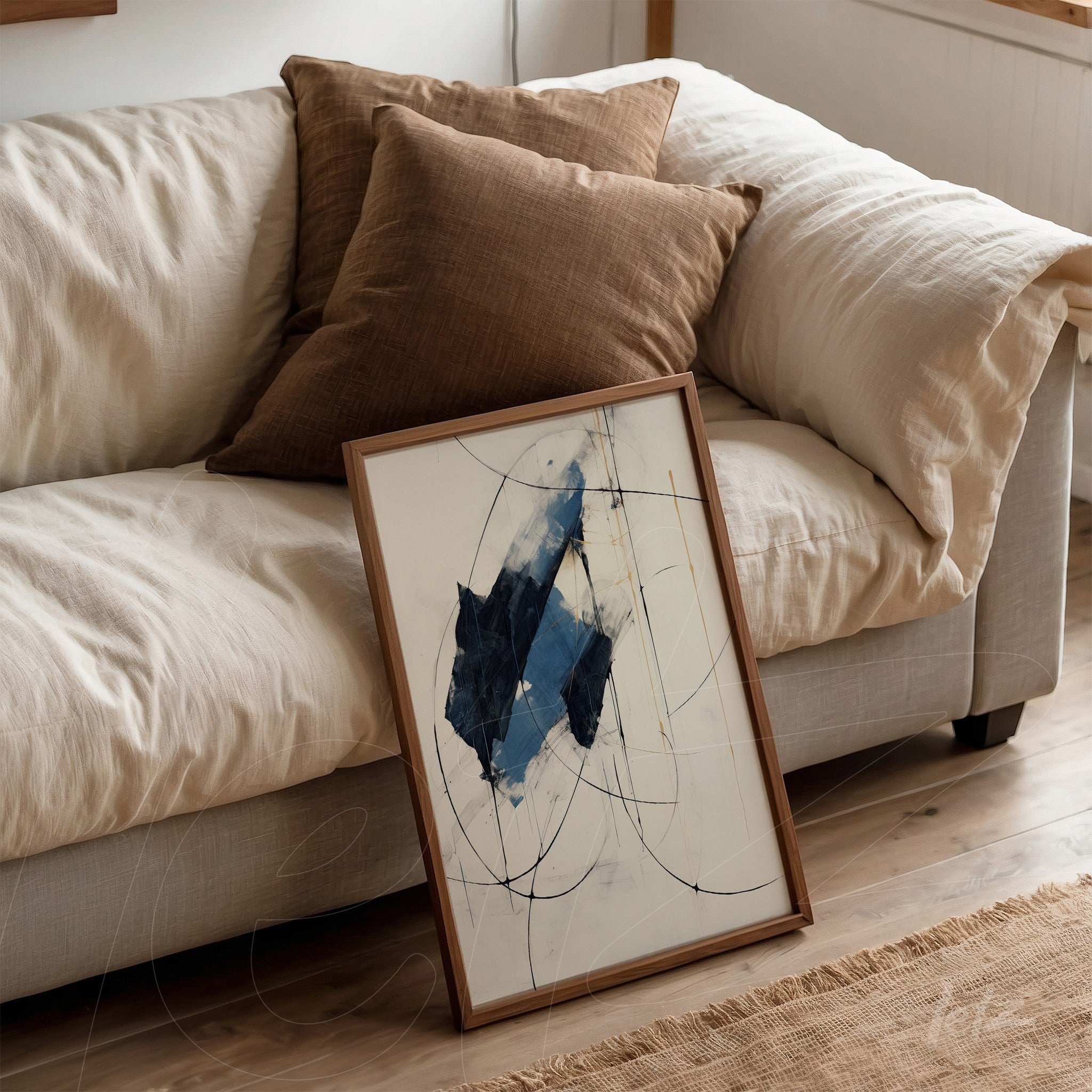 framed abstract artwork in blue and white leaning against a sofa with brown cushions