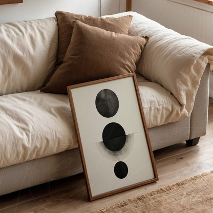 art piece featuring circles in black and gray tones leaning against a light sofa with brown cushions