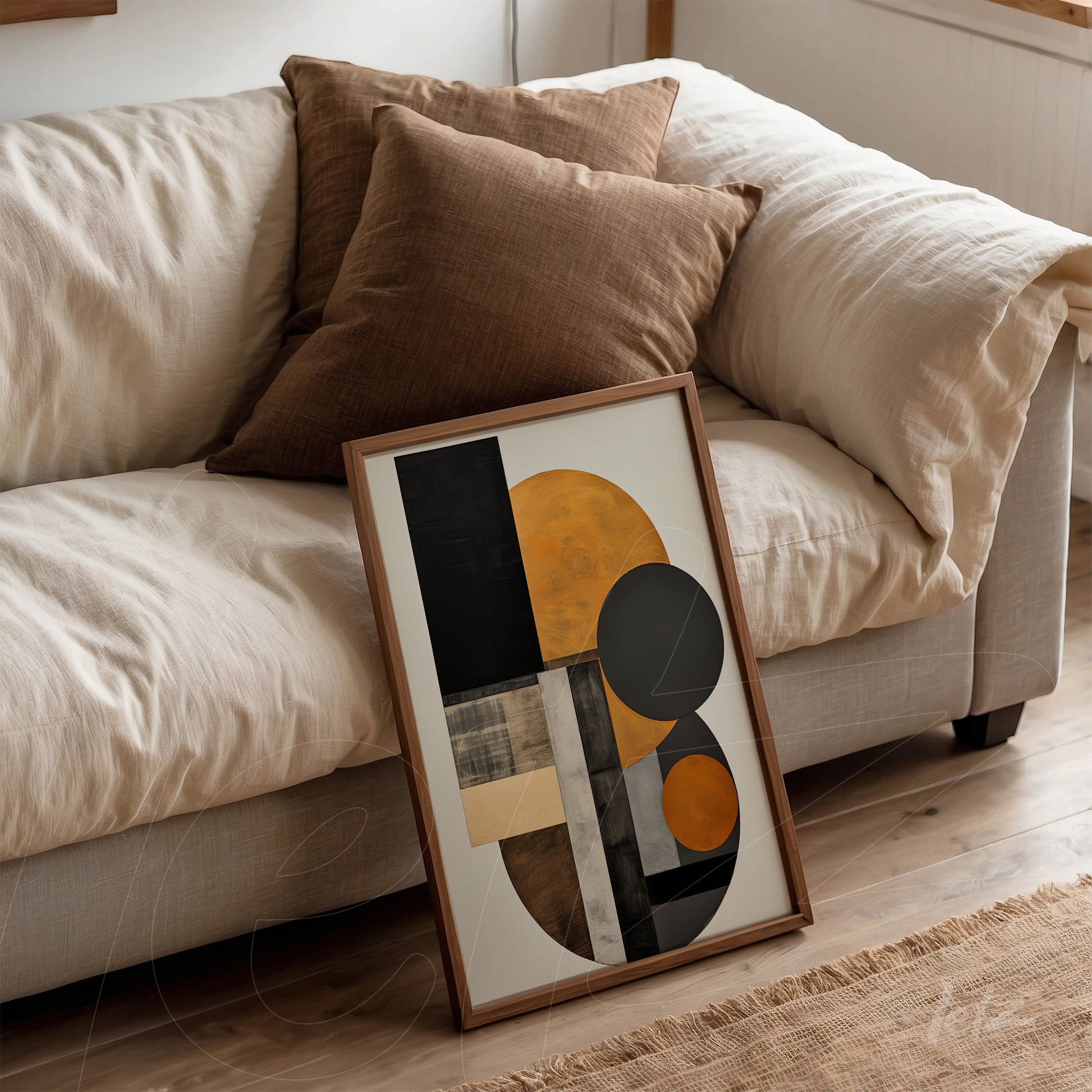 framed decorative art with abstract design in shades of black, gold, and gray, leaning against a light fabric sofa with brown pillows