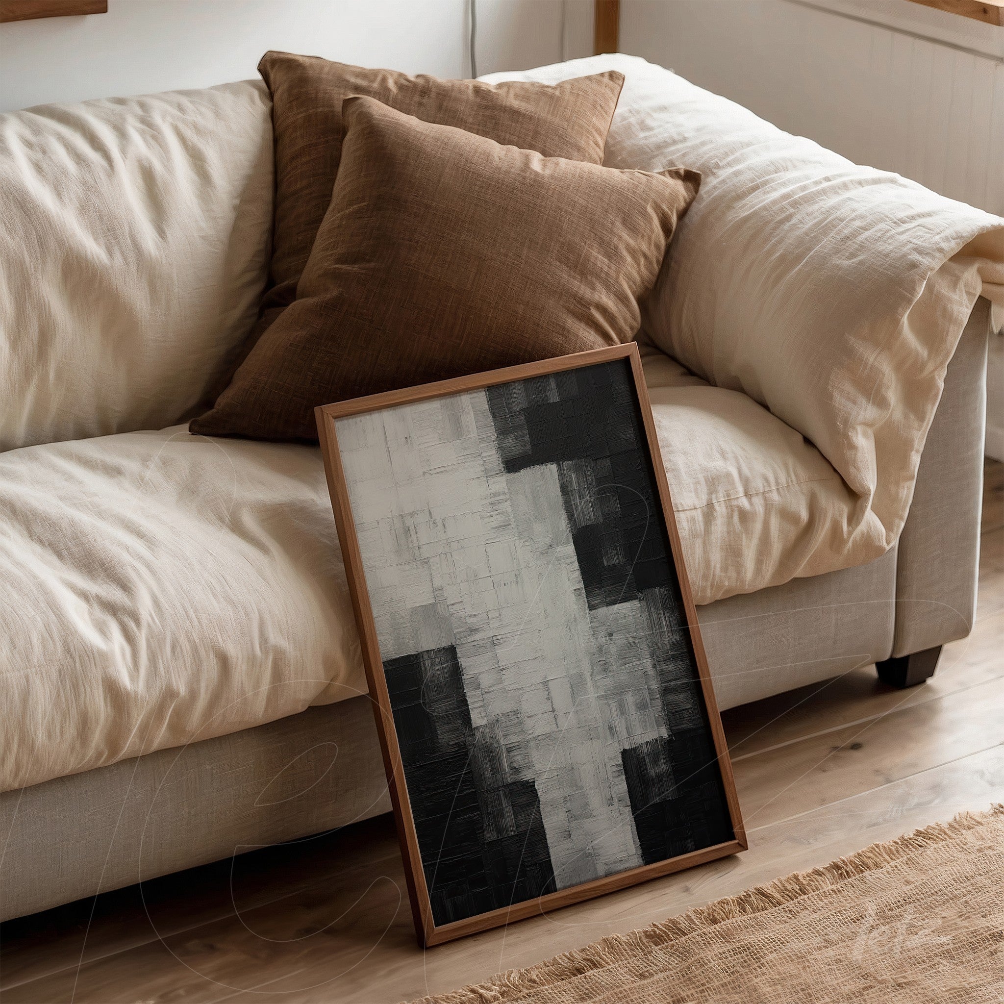 framed abstract art in black and white leaning against a light sofa with brown cushions