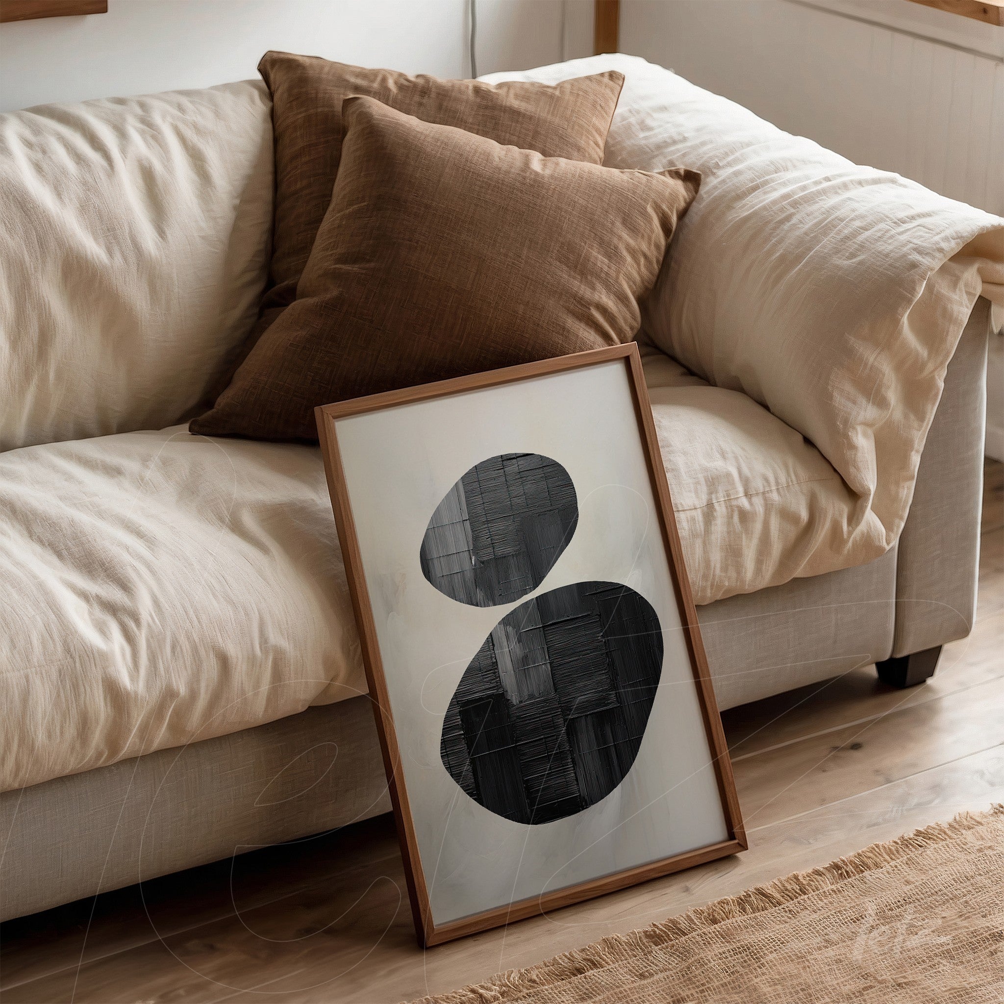 framed wall art featuring black and white abstract shapes with a light wood frame, leaning beside pillows on a beige sofa