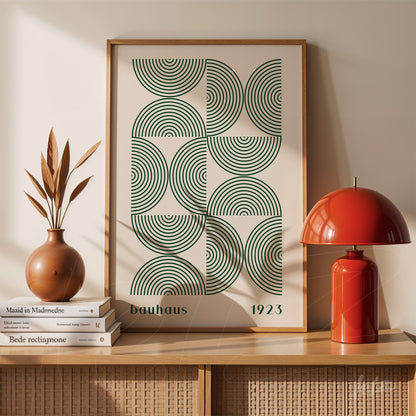 poster print featuring geometric green overlapping circles with the text 'bauhaus 1923', framed in light wood and placed on a wooden sideboard with decorative items beside it