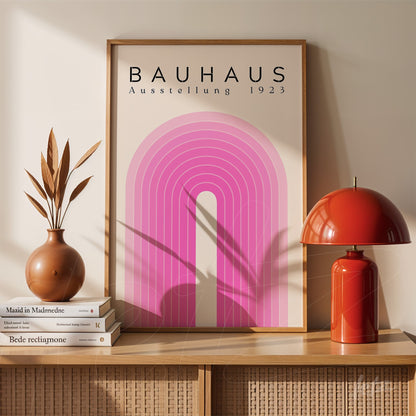 poster print with pink geometric Bauhaus-inspired design framed in light wood, placed on furniture next to red lamp and decorative vase
