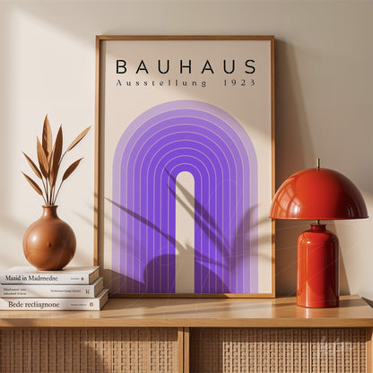 poster with geometric purple design of bauhaus exhibition 1923 framed in light wood displayed on a sideboard with a red lamp and decorative vases