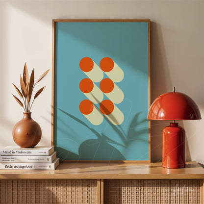 framed geometric illustration with orange circles casting shadows on a blue background, displayed on a shelf with a red lamp and decorative vase
