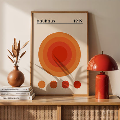 framed geometric bauhaus style art with orange concentric circles displayed on a shelf with a red lamp and decorative vase