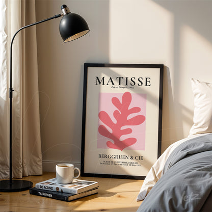 decorative wall art featuring Matisse artwork in black frame leaning against a light-colored wall with natural light and a lamp beside it