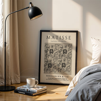 framed line art print featuring stylized faces in a black frame leaning next to a floor lamp in a bright setting