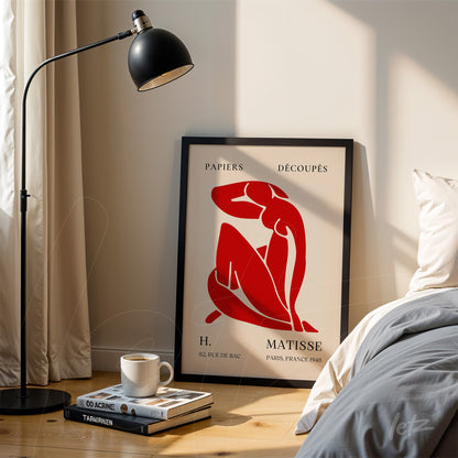 framed wall art featuring a red silhouette on a light background, leaning beside a floor lamp in a bright setting
