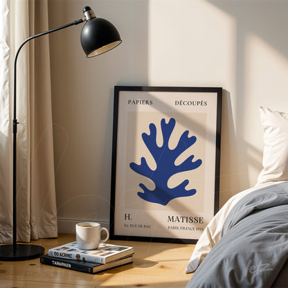 framed modern art print of blue coral in black frame, leaning next to a bed with bedside table