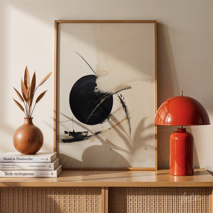 abstract black and white wall art in light wood frame displayed on wooden table with ceramic vase and red lamp