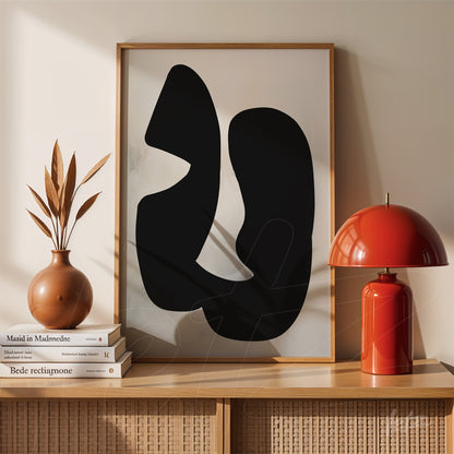 abstract artwork in light wood frame featuring black shapes, placed on wooden shelf with ceramic vase and red lamp