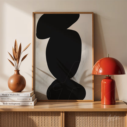 abstract wall art in black framed in light wood frame beside a ceramic vase and red lamp