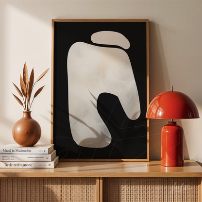 abstract artwork in light wood frame featuring organic shapes on black background displayed on table beside vase and lamp