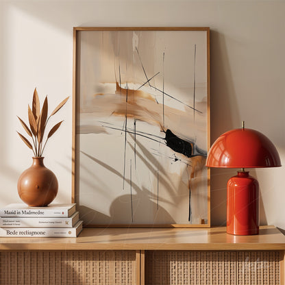 abstract wall art featuring black lines and neutral tones in a light wood frame displayed on a shelf next to a red lamp