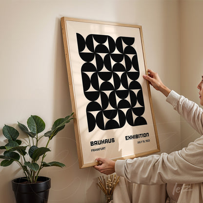 geometric black and white poster framed with light wood, displayed on a neutral wall