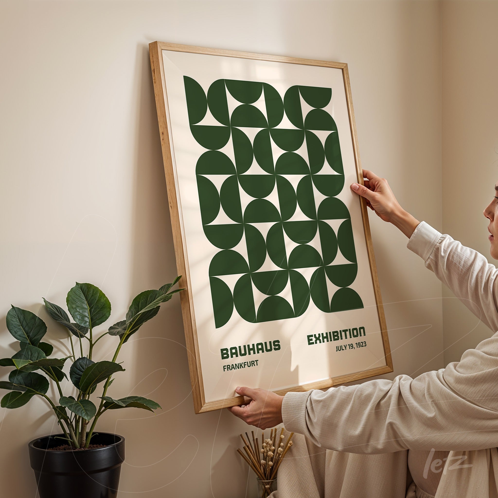 poster print with geometric bauhaus style design in light wooden frame being hung by a person