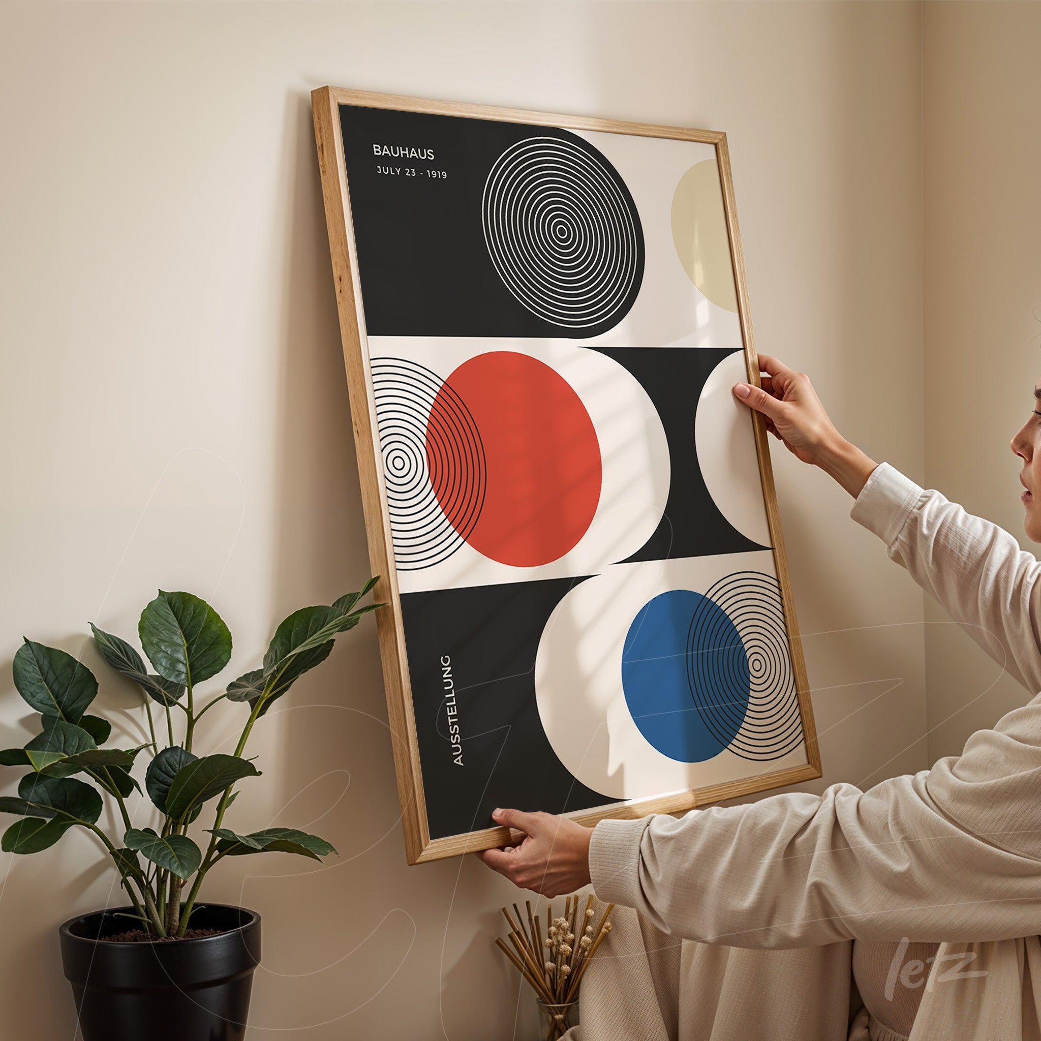 modern Bauhaus-style poster print with colorful circles in black, red, blue, and beige, framed in light wood, leaning against a beige wall