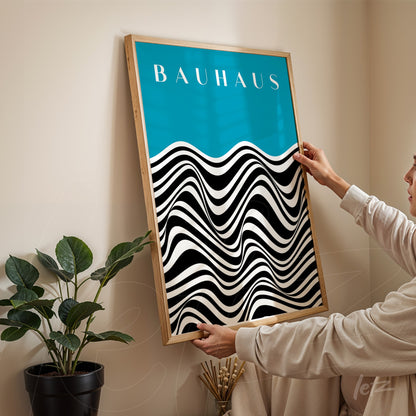 poster with black and white wavy design on blue background featuring 'bauhaus' text, framed in light wood held by person
