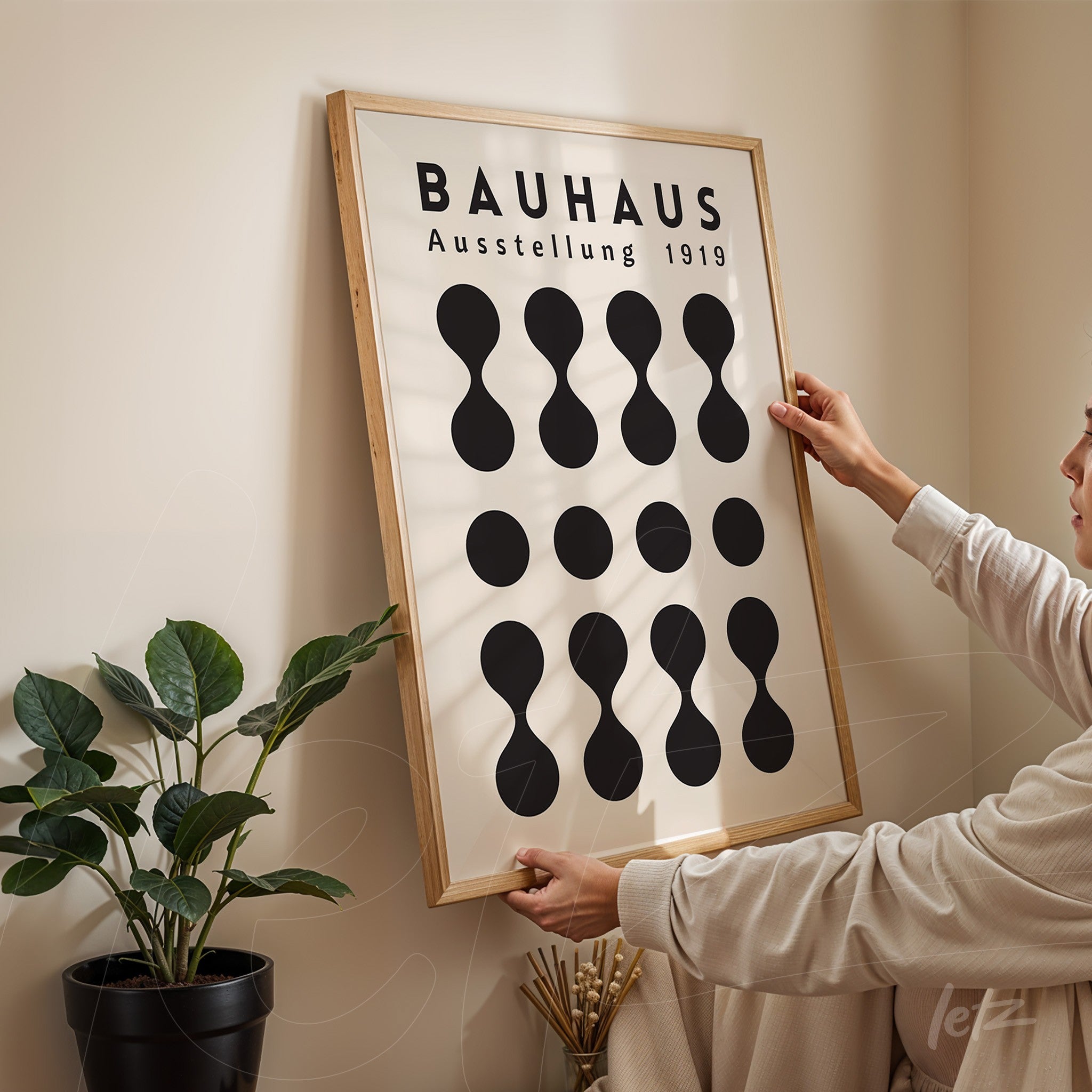 minimalist bauhaus 1919 poster design in a light wood frame being hung on a neutral colored wall