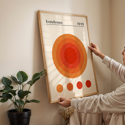 printed poster with geometric design of concentric orange and red circles, dated 1919, framed in light wood, displayed on a beige wall