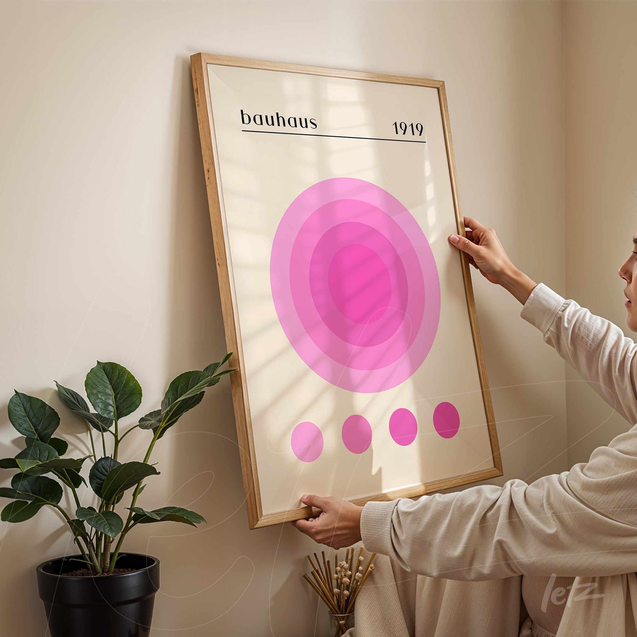 wall art with pink concentric circles and 'bauhaus 1919' title in a light frame, being hung on a beige wall
